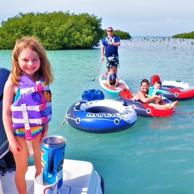 Little girl standing on end of boat with people in inner tubes behind her