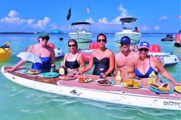 Line of people eating food off of paddleboard in the water