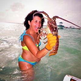 Women holding up huge lobster in the water